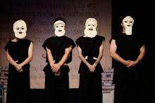 Cuatro actores y actrices de Teatro Paladio en escena, vestidos de negro y con máscaras griegas