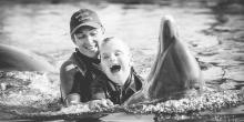 Fotografía del niño Ioan Inchusta feliz nadando con delfines y una monitora